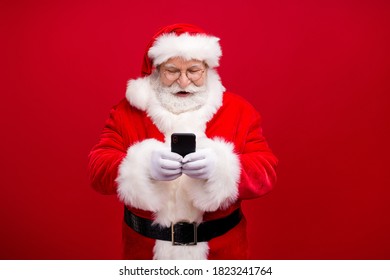 Portrait of his he nice attractive handsome cheerful cheery focused Santa using gadget 5g fast speed blog blogger post comment media isolated over bright vivid shine vibrant red color background
