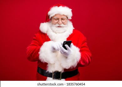 Portrait of his he nice attractive handsome cheerful focused Santa, father using device gadget 5g web service blog post smm comment isolated over bright vivid shine vibrant red color background
