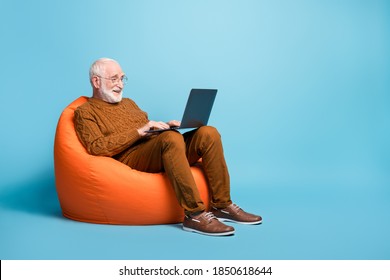 Portrait of his he nice attractive focused bearded grey-haired man sitting in bag chair using laptop writing email letter browsing web wi-fi isolated over blue pastel color background - Shutterstock ID 1850618644