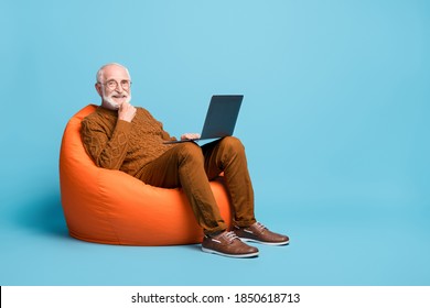 Portrait of his he nice attractive cheerful skilled smart clever bearded grey-haired man sitting in bag chair using laptop calling video isolated over blue pastel color background - Shutterstock ID 1850618713