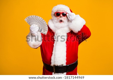Portrait of his he nice attractive amazed astonished fat overweight bearded Santa holding in hand usd cash 100 hundred salary deposit isolated bright vivid shine vibrant yellow color background