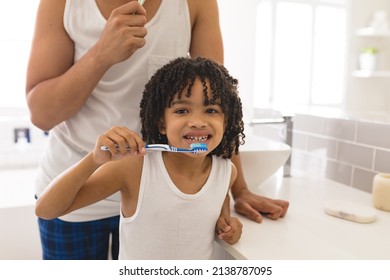 Portrait Of Hispanic Boy Brushing Teeth With Father In Bathroom At Home. Unaltered, Family, Togetherness, Hygiene And Routine Concept.