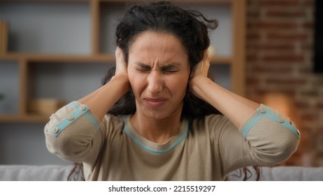 Portrait Hispanic Caucasian woman irritated distraught girl sitting at home covers ears with hands ignores refuses to listen hear protects from noise shouting loud sounds holds head suffers headache