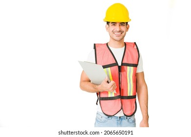 Portrait Of An Hispanic Contractor Wearing A Safety Vest And A Helmet While Using A Clipboard While Working 