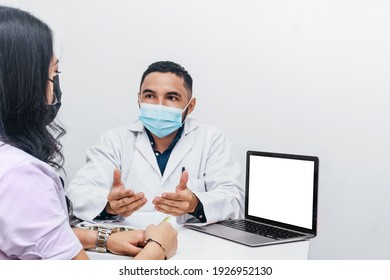 Portrait Of A Hispanic Doctor Or Dentist Wearing A Mask Speaking At An Appointment With A Female Patient. Health And Oral Hygiene Concept.