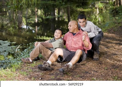 Portrait Hispanic Father And Sons Outdoors By Pond Having Conversation