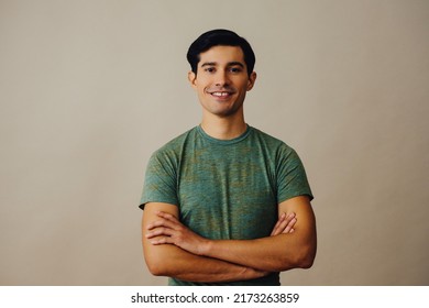 Portrait Hispanic Latino Man With Arms Crossed And Black Hair Smiling Handsome Young Adult Green T-shirt Over Gray Background Looking At Camera Studio Shot