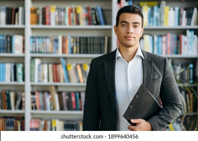 Portrait Of Hispanic Man In Formal Wear At The Workplace. Successful Male Manager Looks At The Camera, Smiling. Influential Businessman Standing In Modern Office, Show Self Confidence