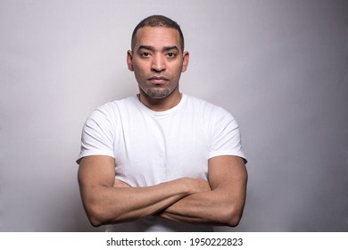 A portrait of a Hispanic middle age athletic man in a white t-shirt, serious, crossed hands, isolated on the grey background