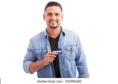 Portrait Of A Hispanic Young Man Dressed Casually And Holding His Favorite Credit Card Against A White Background