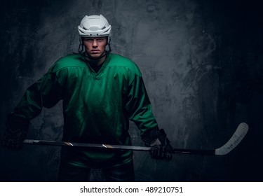 Portrait of a hockey player in protective clothes holds playing stick on grey background.