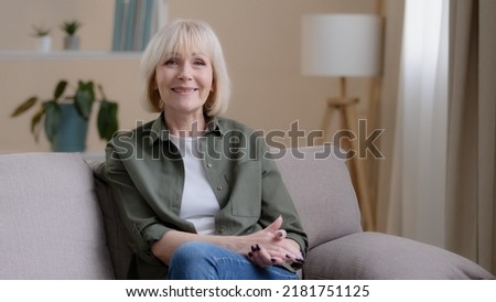 Portrait at home pensive thinking smiling beautiful older adult Caucasian lady looking away at window dreaming turning to camera sit on sofa senior retired woman grandma feel satisfied in living room