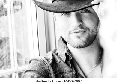 Portrait of hot male cowboy wearing hat sitting in window
