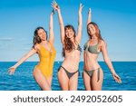 Portrait of hree beauty young women spreading their arms on the sand of beach and looking at camera. Group of only girls in bikinis swimsuit enjoying the coast freely. Summer vacations at shore. High