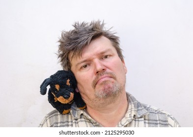 Portrait Of A Humorous Male With A Dog Toy On His Shoulder. A Male With Ruffled, Tangled Hair Presses His Cheek Against The Stuffed Toy. Indoors. Selective Focus.