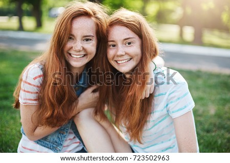 Portrait of identical ginger twin sisters smiling and having fun. Red haired rascals taking the best of their life. Friendship and youth concept.