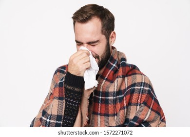 Portrait Of Ill Caucasian Guy Wrapped In Blanket Sneezing And Holding Paper Napkin Due To Flu Isolated Over White Background