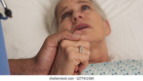 Portrait Of Ill Elderly Woman Lying In Bed Holding Hands With Registered Nurse