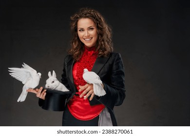 A portrait of a illusionist in a magician's costume and black top hat performing magic tricks with white doves against a dark background - Powered by Shutterstock