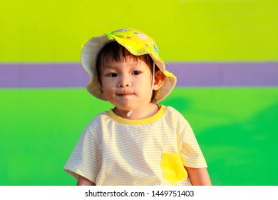 Portrait Image Of 1 Year And 4 Months Old Asian Little Girl In Bright Yellow Outfit With Cute Hat Against Lime Green Background.Concept Of Happy Healthy Kids Travel In Summer Or Child Playing.