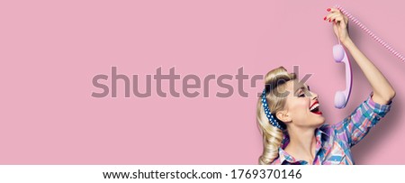 Portrait image - amazed woman holding telephone tube. Excited pin up girl, profile. Retro fashion and vintage concept. Pastel pink rose background. Copy space for some text. Pinup style suit party. 