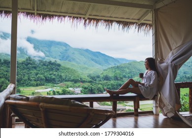 Portrait image of a beautiful asian woman holding and drinking hot coffee on balcony , looking at mountains and green nature  - Powered by Shutterstock