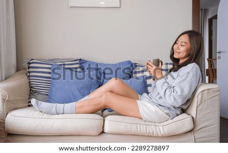 Portrait image of a beautiful woman with closed eyes while drinking hot coffee and relaxing on a sofa at home