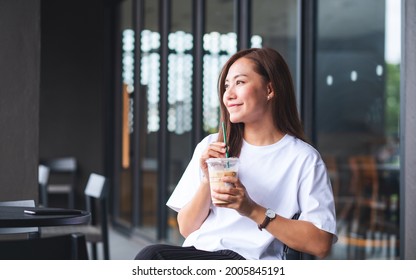 Portrait image of a beautiful young asian woman holding and drinking iced coffee in cafe - Powered by Shutterstock