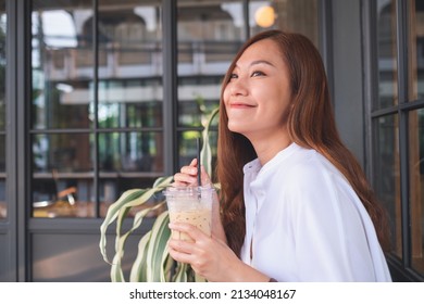 Portrait image of a beautiful young asian woman holding and drinking iced coffee - Powered by Shutterstock