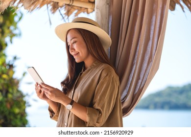 Portrait image of a beautiful young asian woman holding and using mobile phone by the sea - Powered by Shutterstock