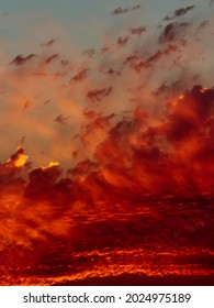 portrait image of a clear turquoise sky covered by tufts of scarlet cloud, some backlit by the twilight light.