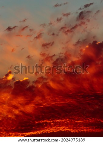 portrait image of a clear turquoise sky covered by tufts of scarlet cloud, some backlit by the twilight light.