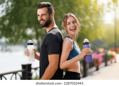 Portrait image of happy smiling, excited couple holding plastic water bottles, woman with man or bearded coach trainer, after successful training, outdoors. Fitness, sport, workout concept. - Powered by Shutterstock