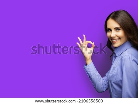 Portrait image of happy smiling showing okay ok hand sign gesture businesswoman, over violet purple background, copyspace. Young cheerful brunette woman in blue cloth at studio ad concept. Executive.