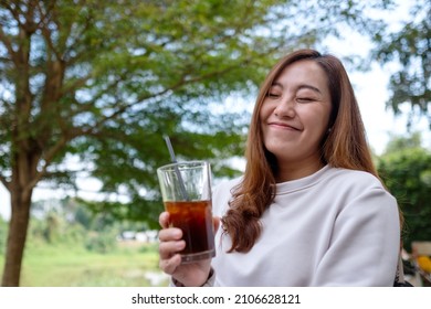 Portrait image of a happy woman holding and drinking iced coffee in the outdoors - Shutterstock ID 2106628121