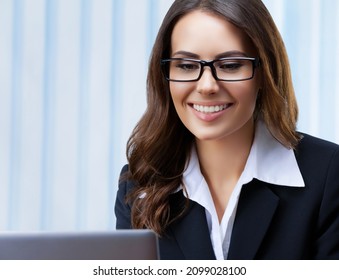 Portrait Image Of Smiling Businesswoman In Black Suit And Spectacles, Working With Laptop Computer At Office. Success In Business, Job And Education Concept. Skype Zoom Video Conference