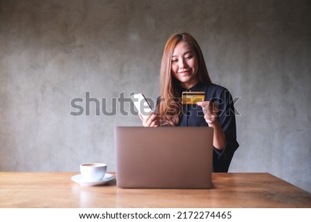 Portrait image of a woman holding credit card while using smart phone and laptop for online shopping