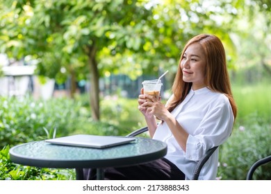 Portrait image a young asian woman holding and drinking iced coffee with laptop on the table in the outdoors - Powered by Shutterstock