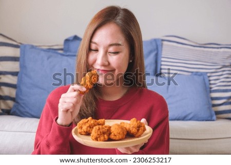 Portrait image of a young woman holding and eating fried chicken in the kitchen at home