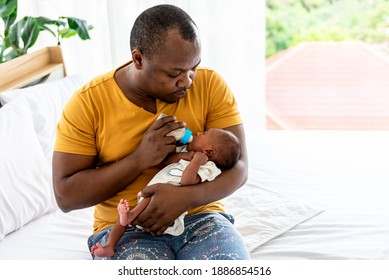 Portrait Images Of  African Father Sitting On Bed, And Feed Milk From Bottle Milk To His 12-day-old Baby Newborn Son, To Family And Food For Infant Concept.