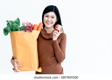 Portrait images of Asian attractive Woman holding paper bag which contains food and fresh vegetables On white background, to people shopping online and new normal concept.