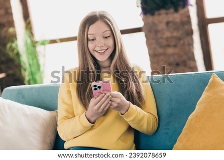 Portrait of impressed pleasant person with long hairstyle wear stylish sweatshirt look at smartphone read interesting post inside house