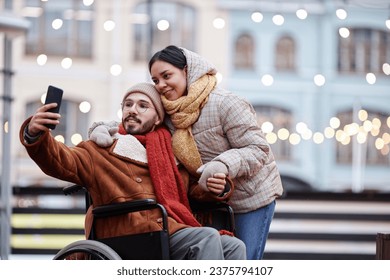 Portrait of inclusive young couple taking selfie photo outdoors in winter and using smartphone - Powered by Shutterstock