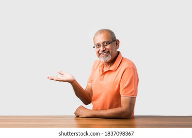 Portrait of Indian asian senior man sitting at table presenting or in success pose