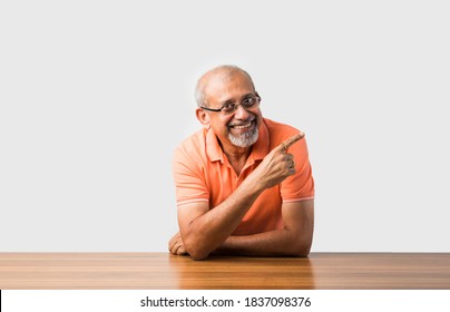 Portrait of Indian asian senior man sitting at table presenting or in success pose