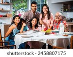 Portrait of Indian family of three generations eating meals together at home looking at camera