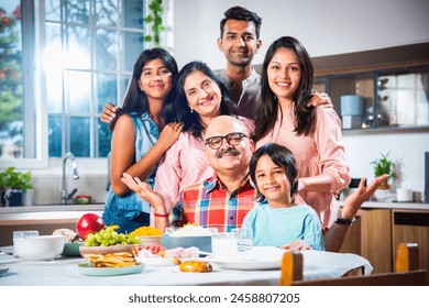 Portrait of Indian family of three generations eating meals together at home looking at camera - Powered by Shutterstock