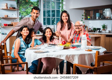 Portrait of Indian family of three generations eating meals together at home looking at camera - Powered by Shutterstock