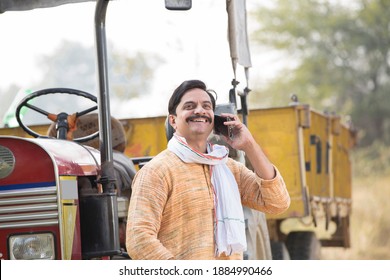 Portrait of Indian farmer talking on mobile phone by tractor