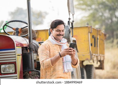 Portrait of Indian farmer talking on mobile phone by tractor